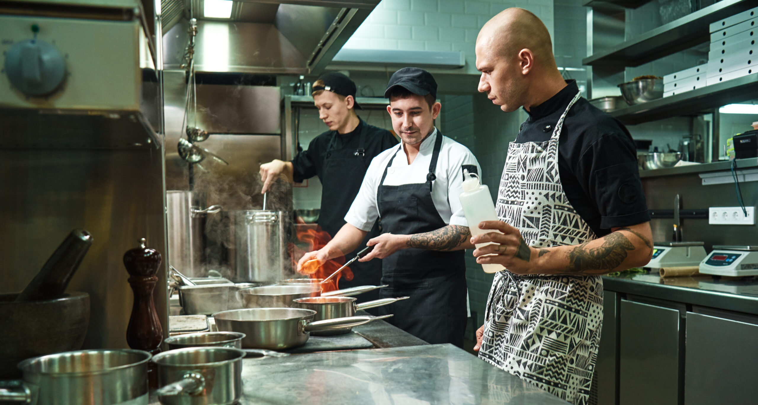 Dangerous work. Profesional chef teaching his two young trainees how how to flambe food safely. Cooking techniques MANIPULACIÓN DE ALIMENTOS DE ALTO RIESGO 100% ONLINE